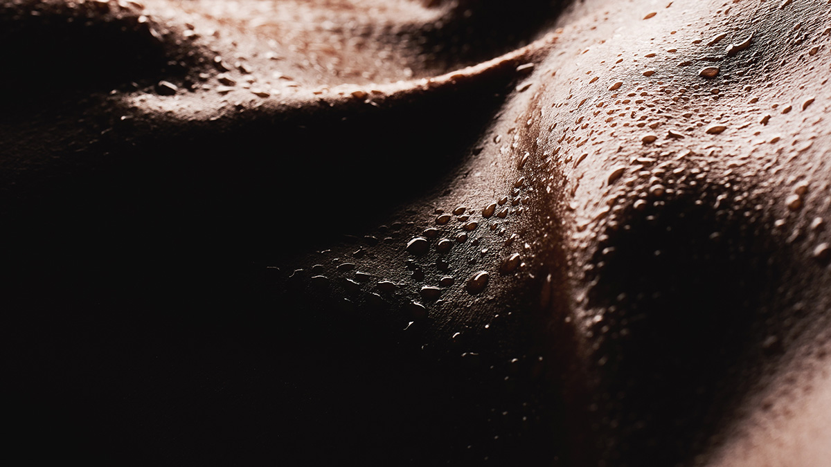 A dark closeup bodyscape with beautiful curves and  skin covered in water droplets 